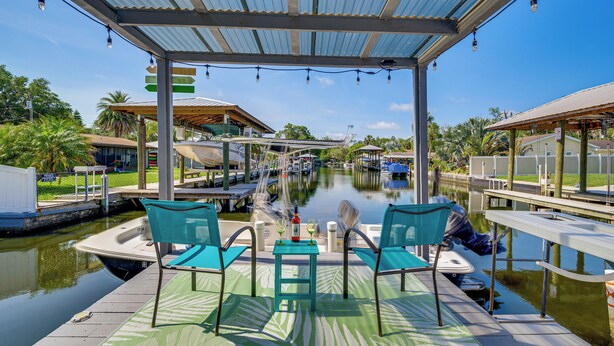 A covered dock with two chairs and a table, overlooking a canal with boats and houses in the background. - Boat Dock & Kayaks: Canalfront Home in Homosassa (Homosassa)