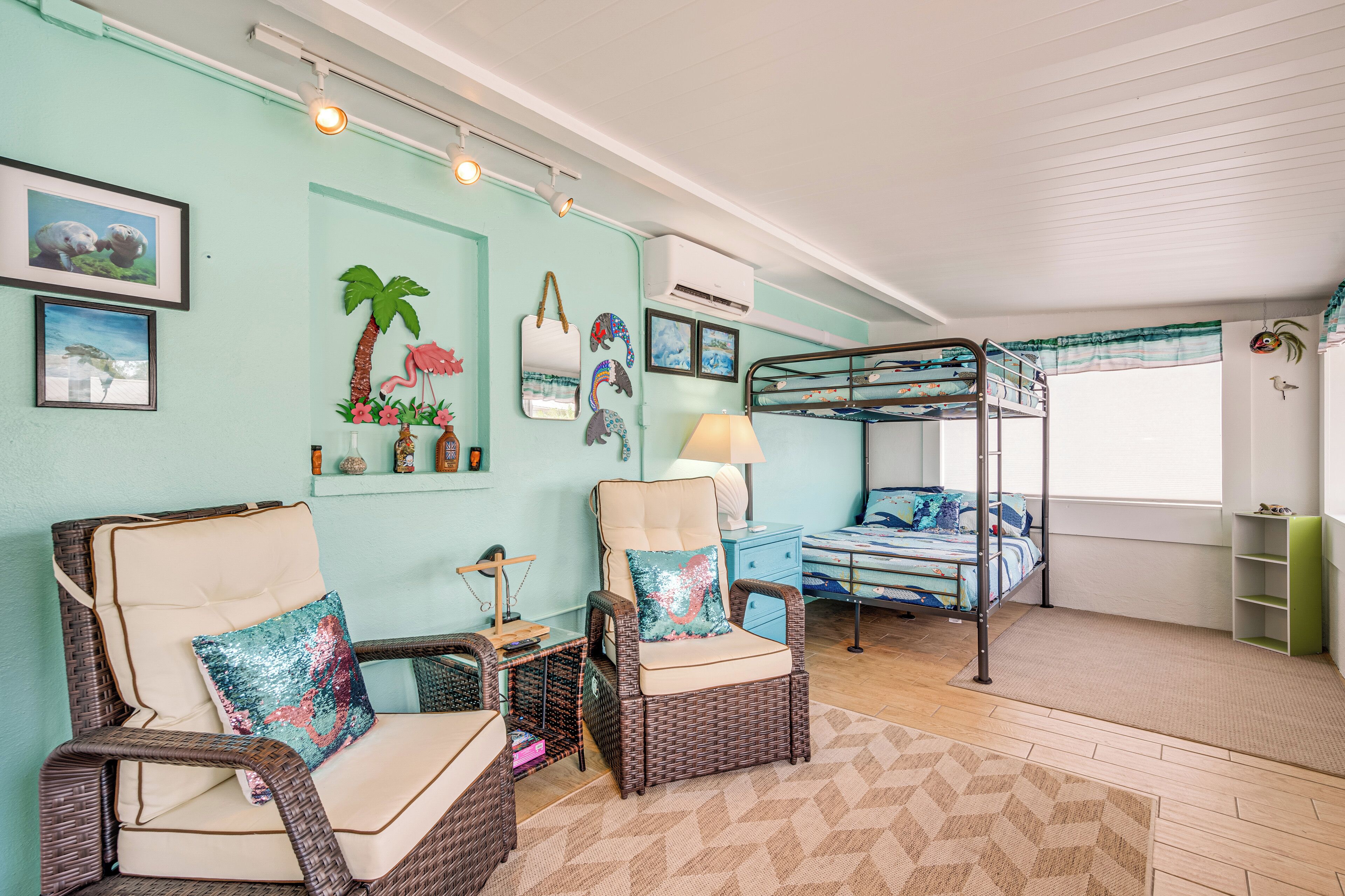A room with a bunk bed, two wicker chairs, a small table, and a lamp.