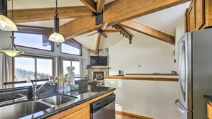 Une cuisine dotée d’un plan de travail en granit, d’un évier en acier inoxydable et d’un lave-vaisselle encastré. Le plafond est en bois, avec des poutres apparentes, et il y a un ventilateur de plafond.