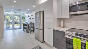 Una cocina moderna con electrodomésticos de acero inoxidable, un comedor con mesa y sillas, y vistas al exterior a través de puertas de vidrio.