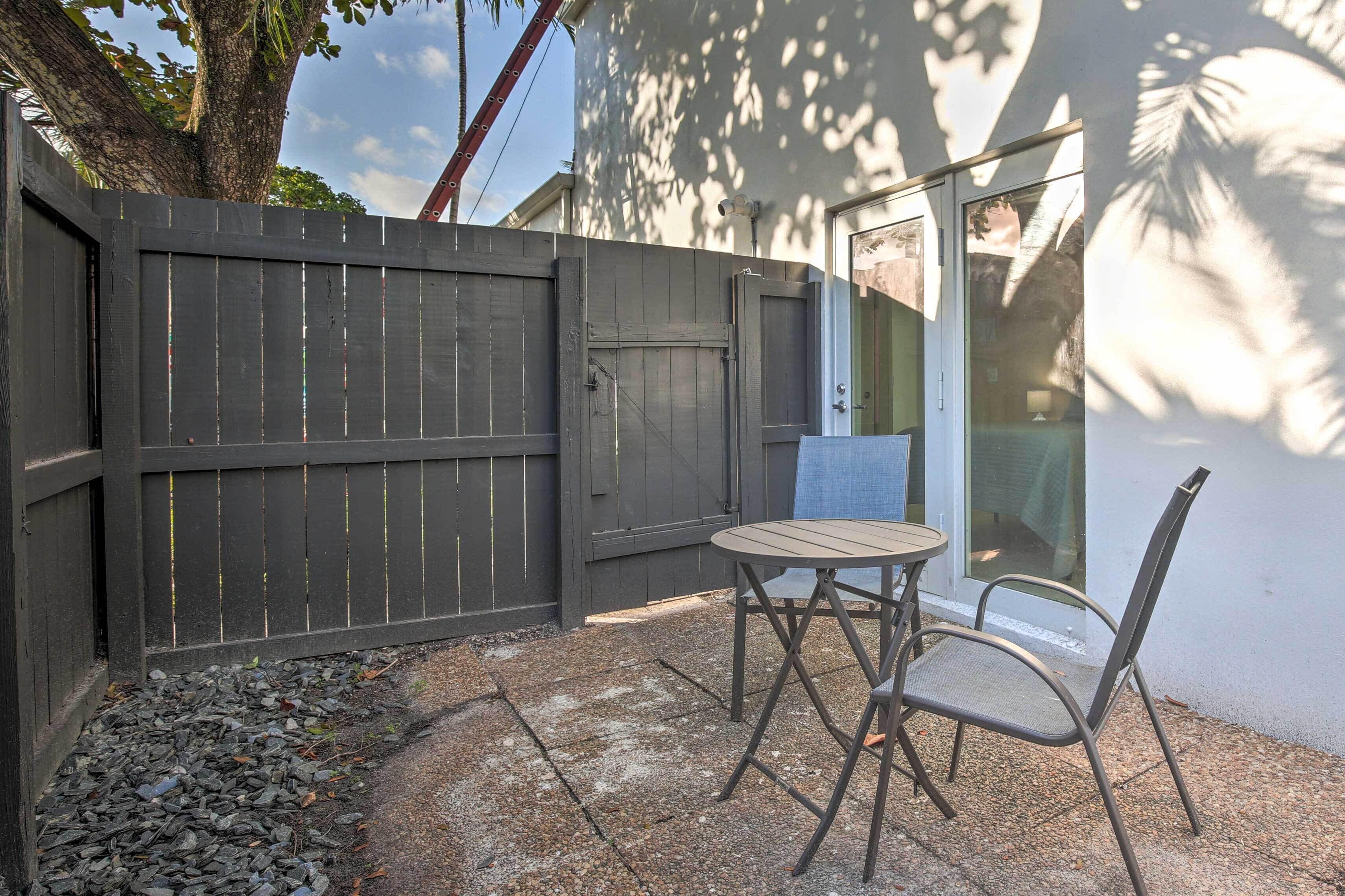 A patio area with a table and chairs, a wooden fence, and a glass door leading to a covered outdoor space.