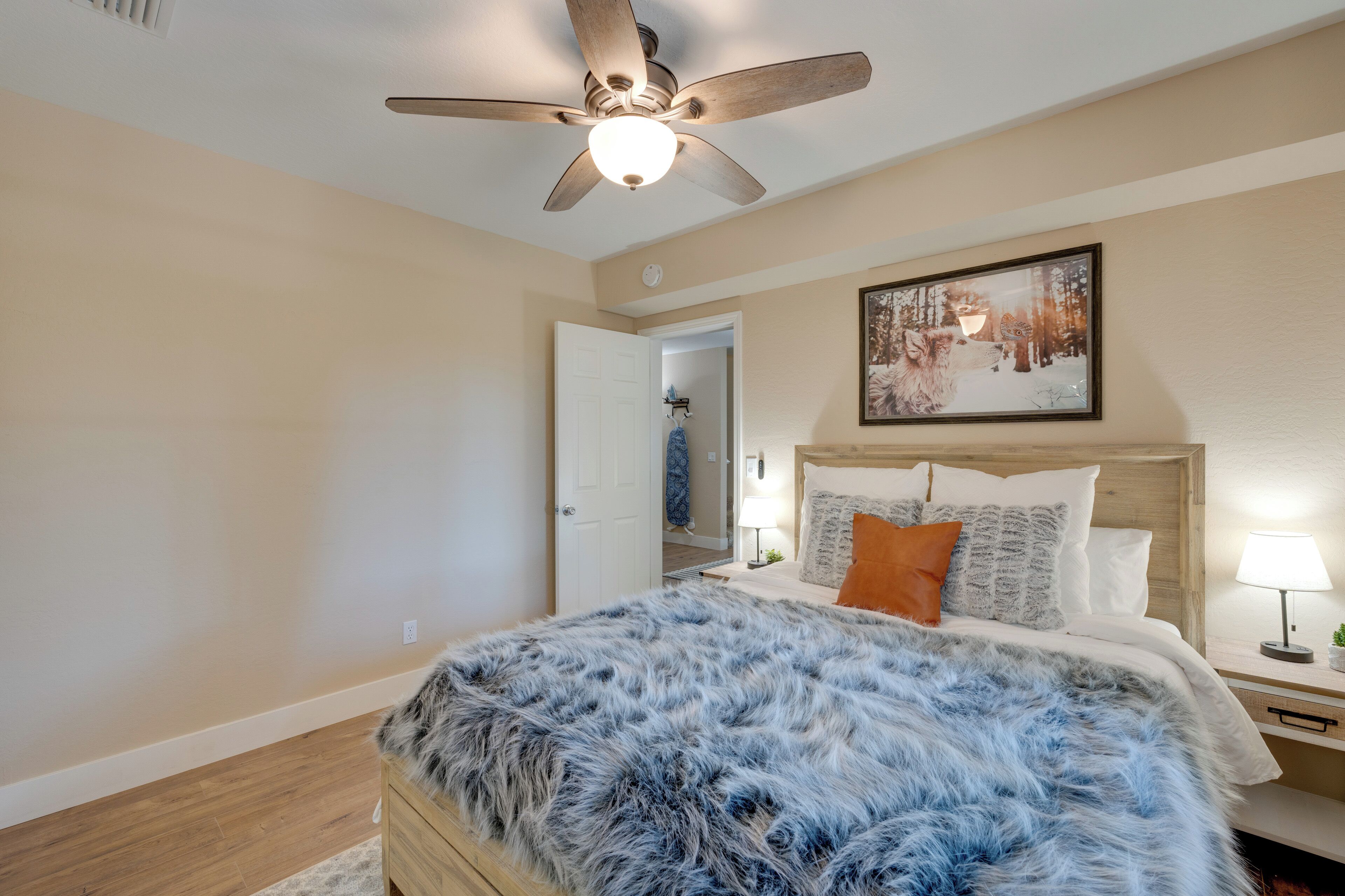 A bedroom with a wooden bed, a ceiling fan, a framed picture on the wall, and a nightstand with a lamp.