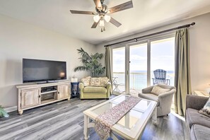 A living room with a flat-screen TV, a ceiling fan, a sofa, a coffee table, and a balcony with a view. - Oceanfront Panama City Beach Condo w/ Pool Access! (Panama City Beach)