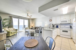 A modern kitchen with white cabinets, a microwave, and an oven. There is a dining area with a wooden table and chairs. - Oceanfront Panama City Beach Condo w/ Pool Access! (Panama City Beach)