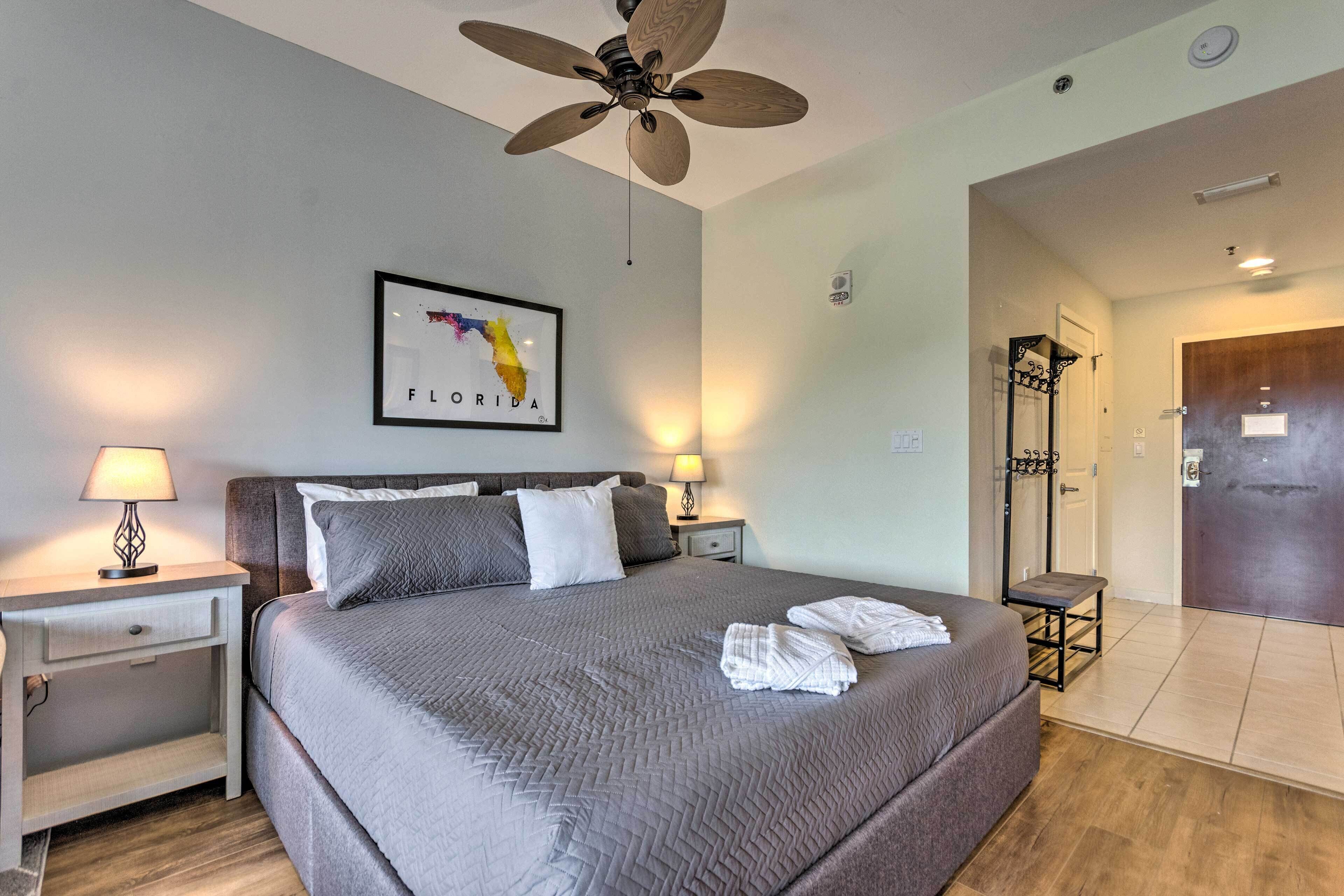 A hotel room with a large bed, two bedside tables with lamps, a ceiling fan, a framed map of Florida, and a wooden door.