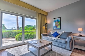 A modern living room with a sofa, a coffee table, and a view of greenery through large windows.