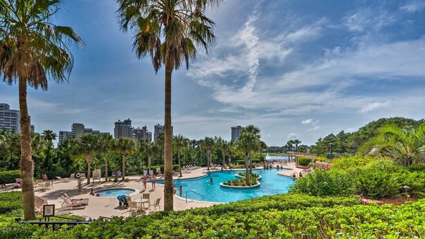 Um resort com várias piscinas rodeado por palmeiras e vegetação, com um horizonte urbano ao fundo.
