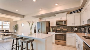 A modern kitchen with white cabinets, stainless steel appliances, and a central island with bar stools. - 6 Mi to Disney: Resort Hideaway w/ Pool Access! (Kissimmee)