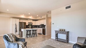 A modern kitchen with white cabinets, a central island, and a dining area with bar stools. - 6 Mi to Disney: Resort Hideaway w/ Pool Access! (Kissimmee)