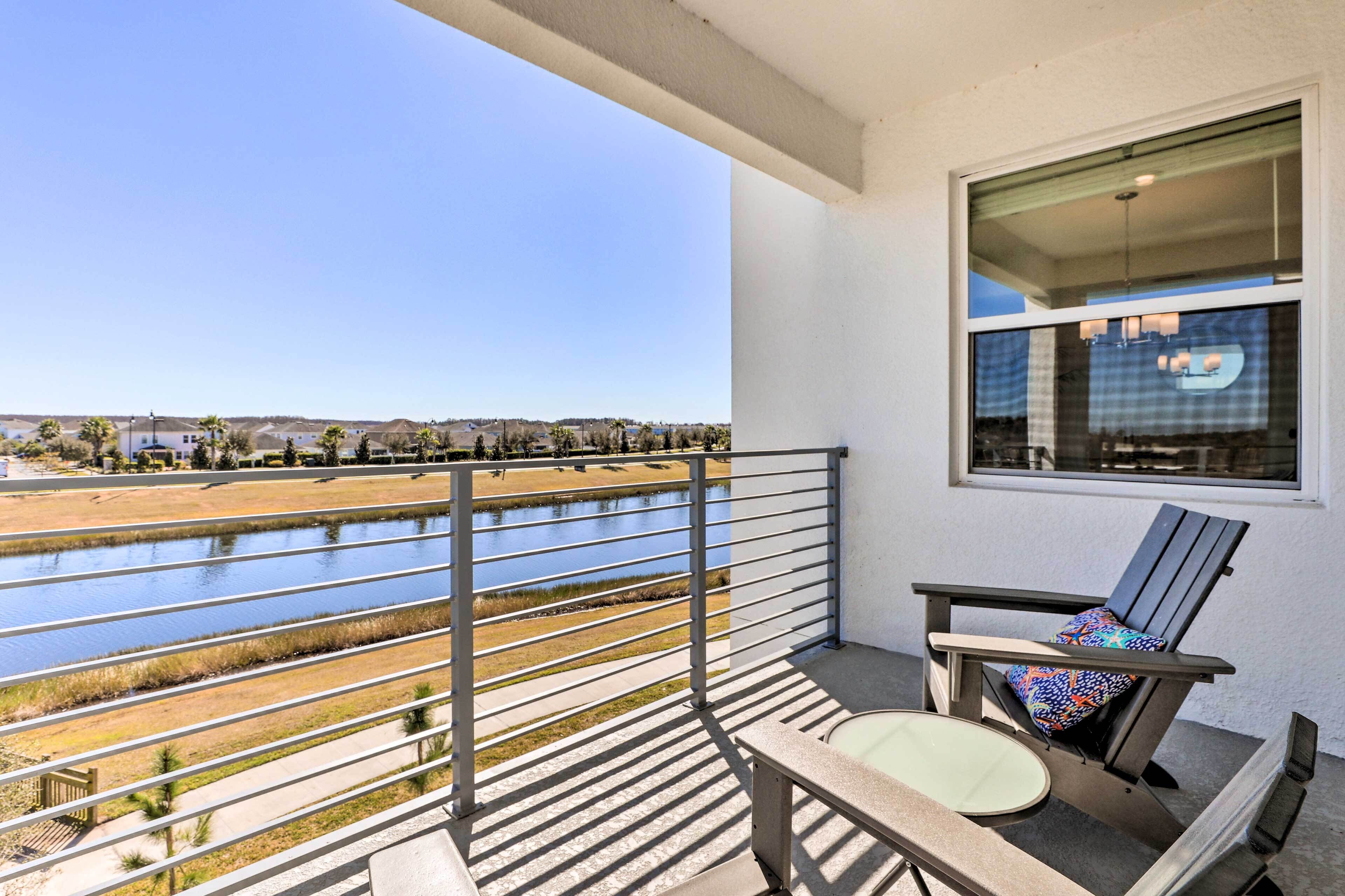 A balcony with a view of a water body and distant buildings, a chair, and a table.