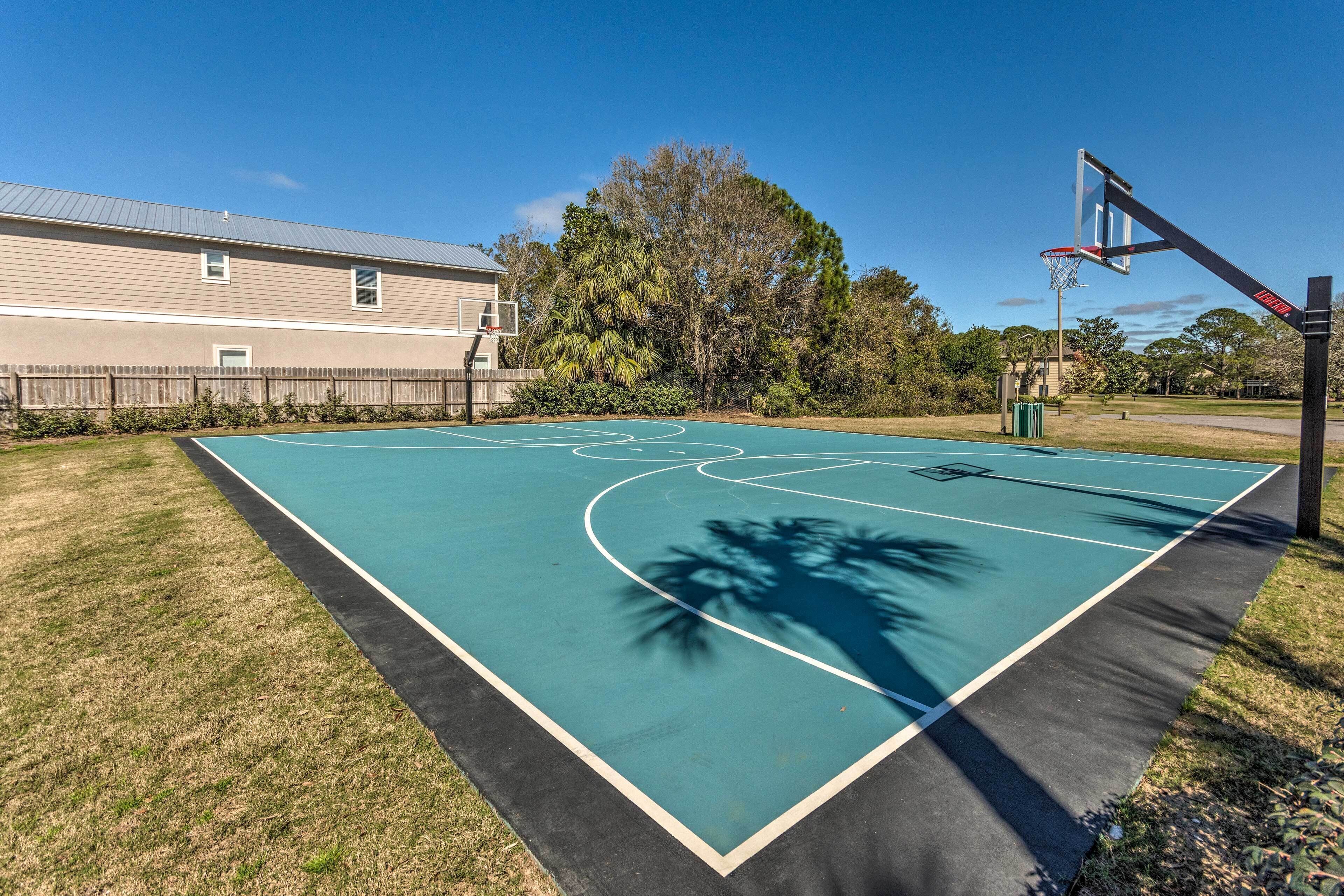 An outdoor basketball court with a wooden fence, a basketball hoop, and a building in the background.
