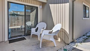 A covered patio with two white plastic chairs and a glass sliding door leading to a backyard.