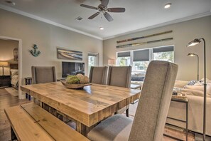 A dining area with a wooden table, cushioned chairs, a ceiling fan, and a view of the outdoors through large windows.