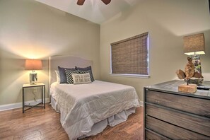 A bedroom with a bed, a nightstand, a dresser, a window with blinds, and a ceiling fan.