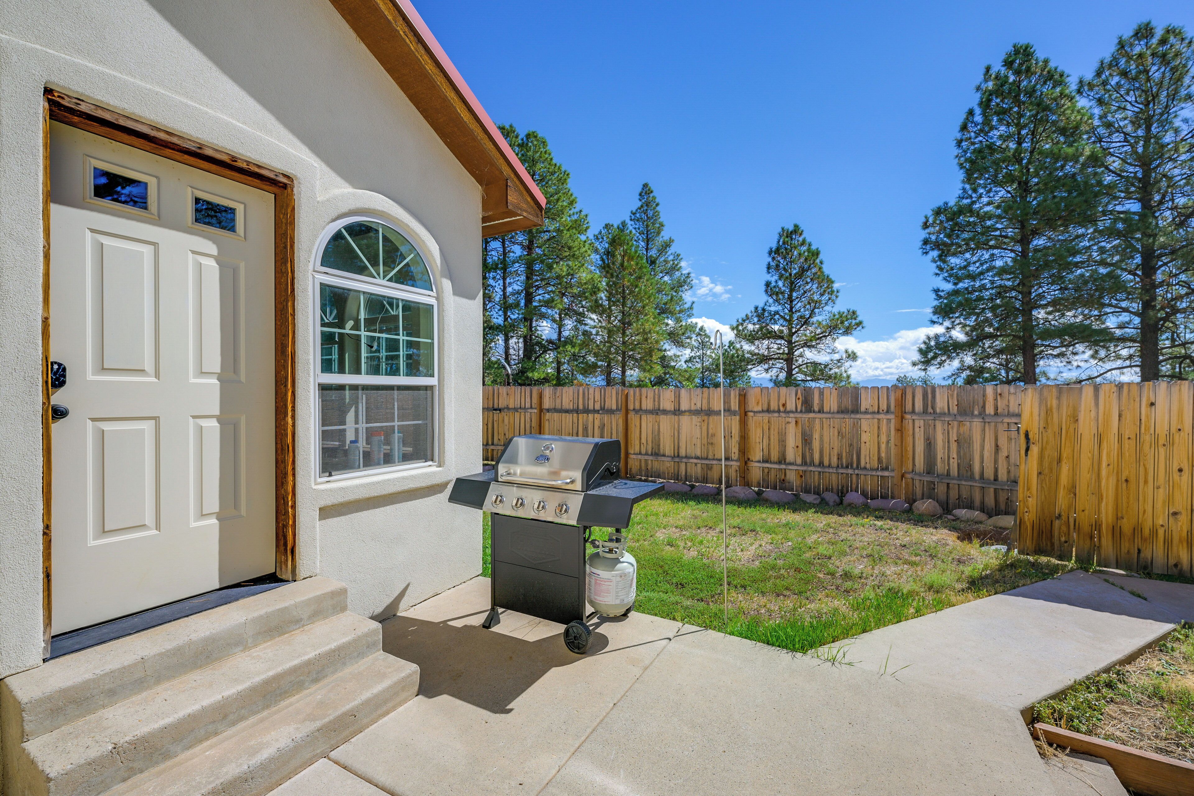 A house with a barbecue grill in the backyard, a wooden fence, and a clear blue sky.