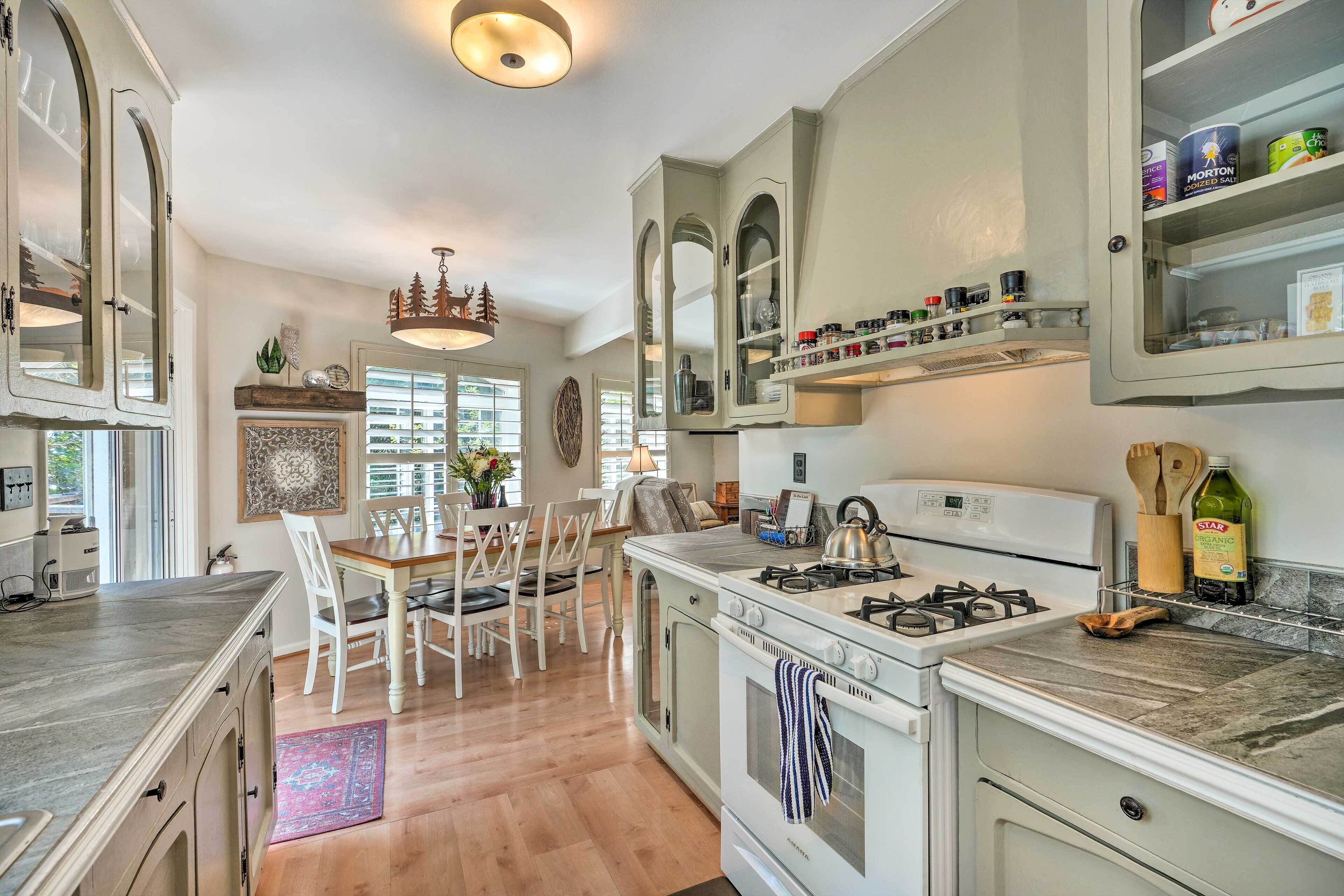A kitchen with white cabinets, a gas stove, and a dining area with white chairs and a table.