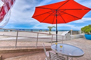 A beachside patio with a red umbrella, a table with a drink, and a view of the ocean. - Oceanfront Luxury Renovated Resort Getaway! (Fort Lauderdale)