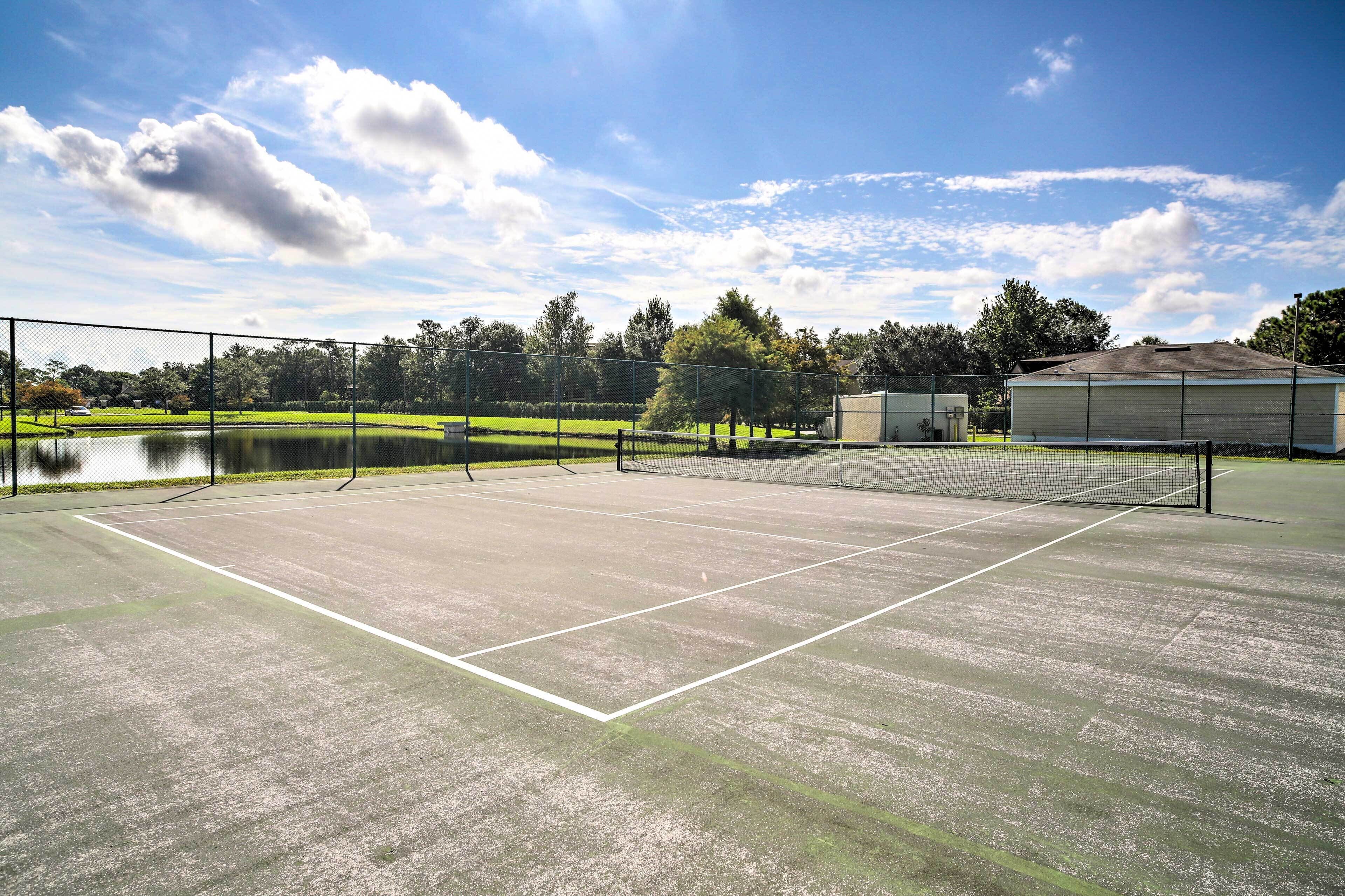 Tenniskenttä, jossa on verkko, ja kentän ympärillä on aita. Taustalla näkyy rakennus.