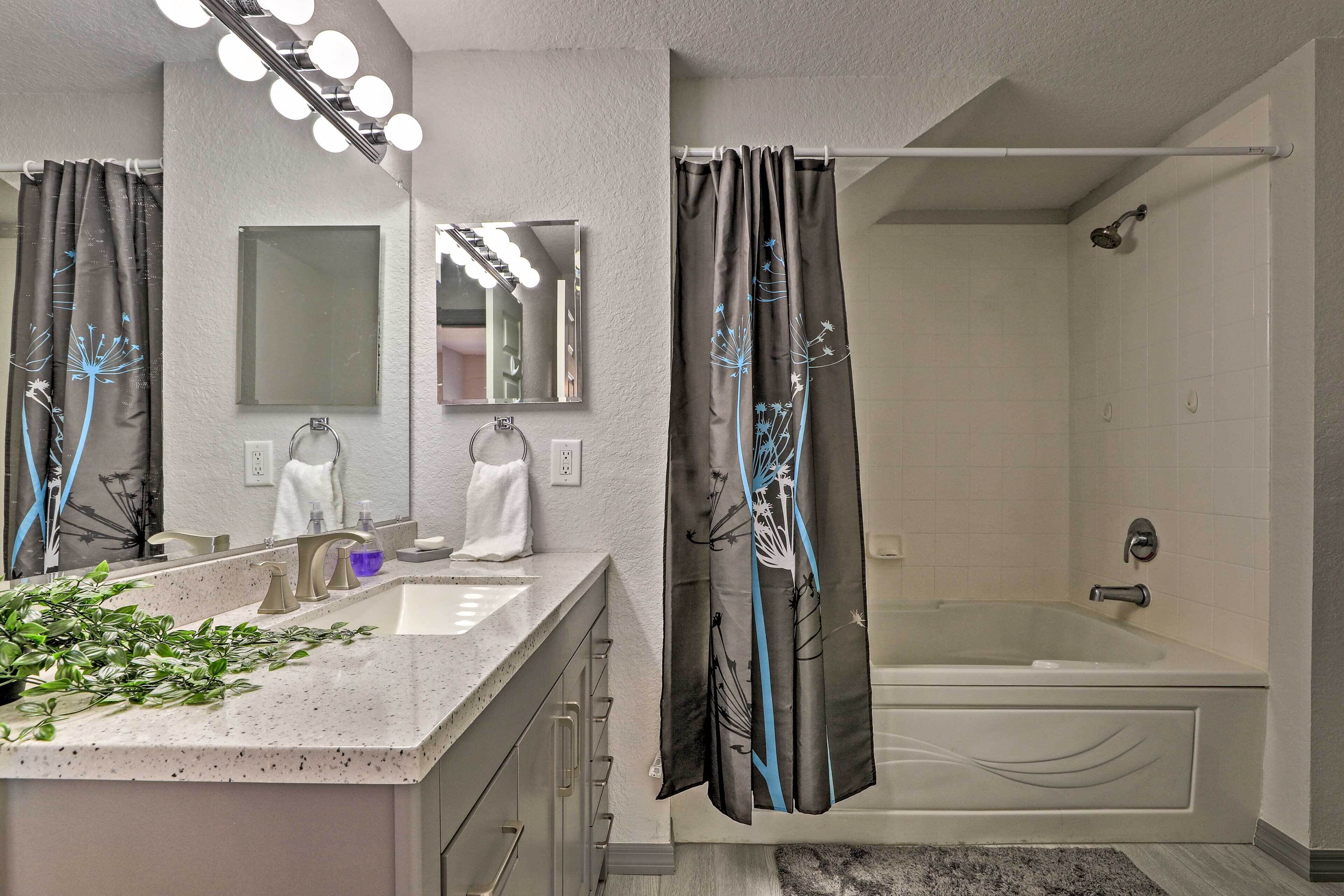 Une salle de bain avec une baignoire, un lavabo avec un miroir et un rideau de douche orné d’un motif d’arbre.