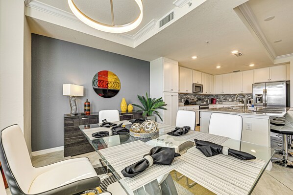 Un espace repas moderne avec une table en verre, des chaises blanches et un élément décoratif mural.