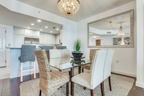 A modern dining area with a glass table, woven chairs, and a chandelier.