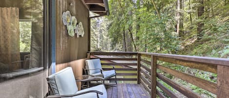 A wooden deck with chairs and a railing overlooking a forested area.