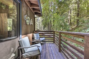 A wooden deck with chairs and a railing overlooking a forested area.