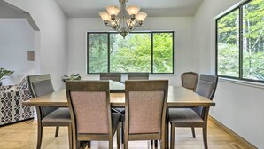 A dining area with a large table, six chairs, and a chandelier. There are large windows with a view of trees. - Tranquil Guerneville Home w/ Redwood Views (Guerneville)