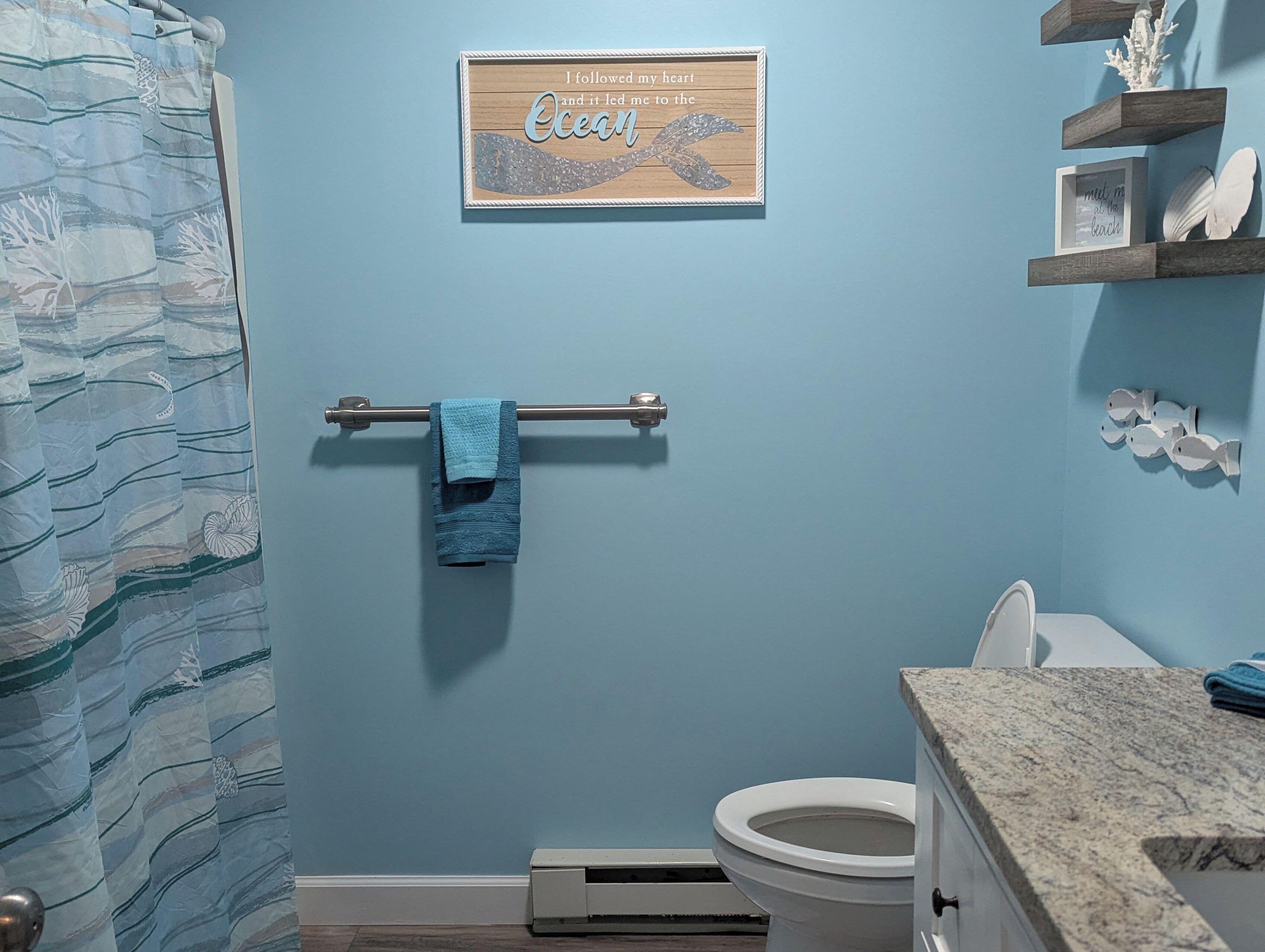 Une salle de bain avec un rideau de douche, un porte-serviettes avec une serviette, des toilettes et un panneau en bois accroché au mur.