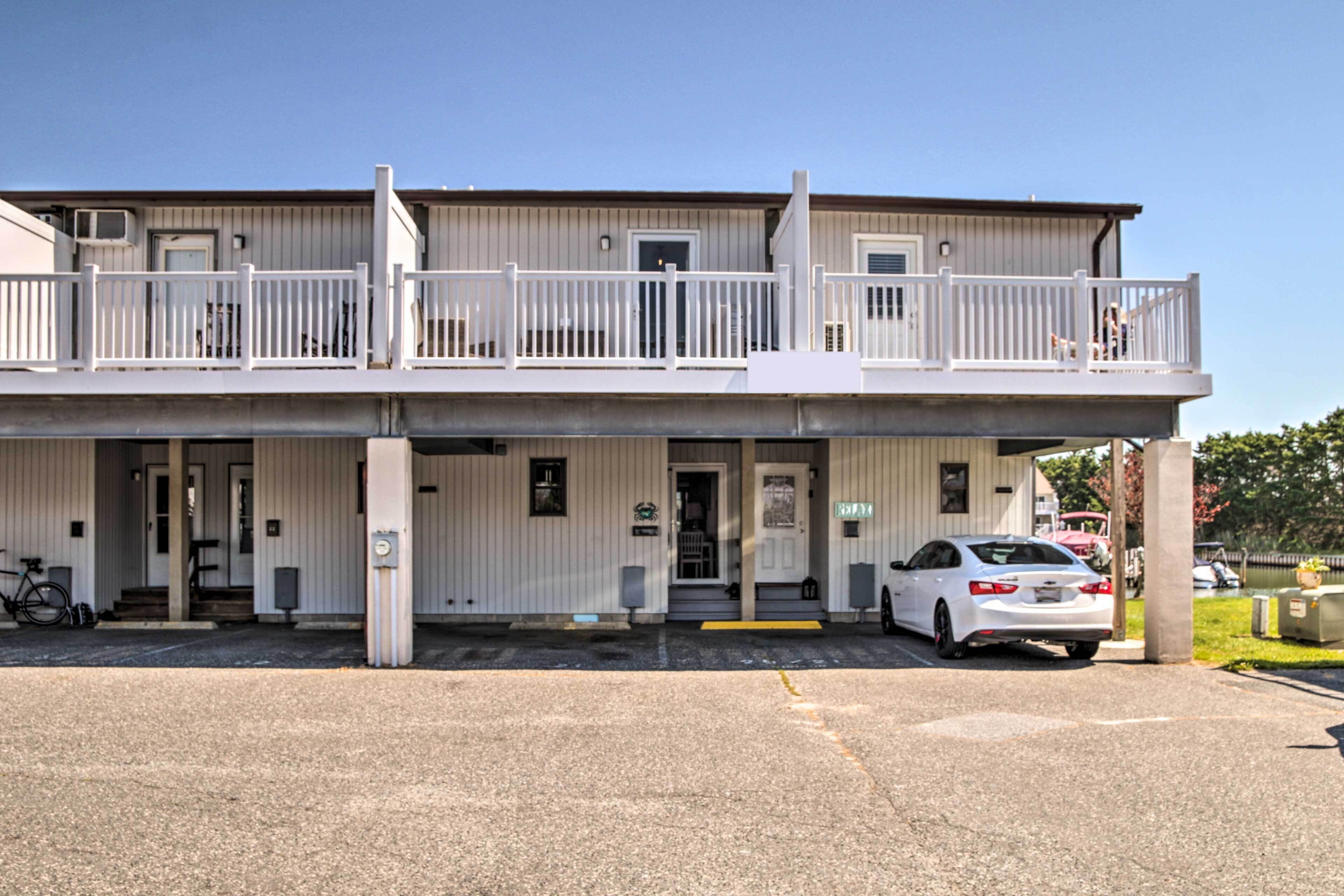 Ein zweigeschossiges Motel mit einem Balkon im Obergeschoss, einer überdachten Einfahrt und einem Parkplatz mit einem weißen Auto.