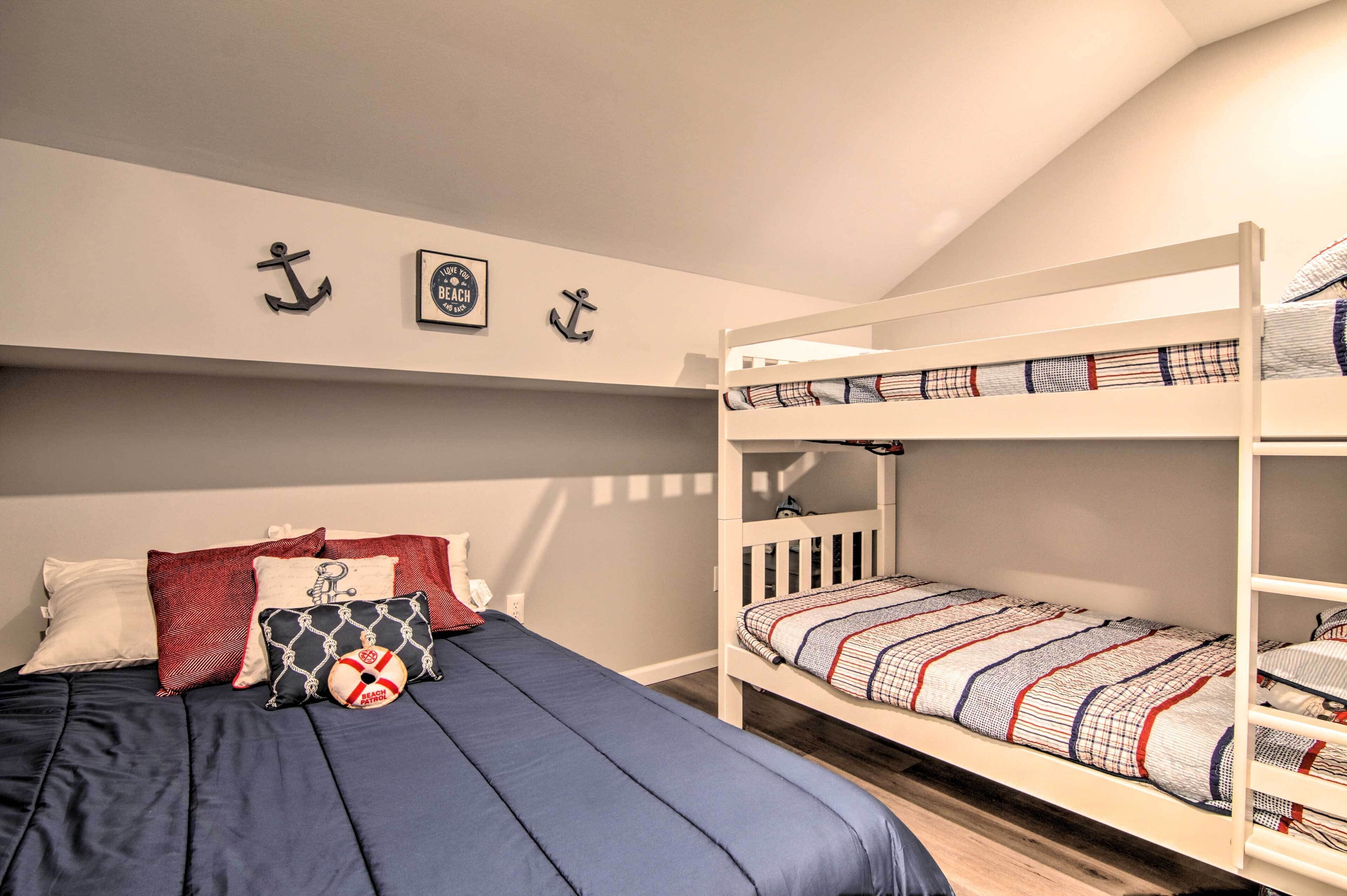 Quarto com beliche, cama azul-marinho, almofadas vermelhas e brancas, e decoração náutica.