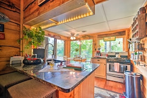 A rustic kitchen with wooden walls, a granite countertop, and a central island. There are wooden cabinets, a stove, and a sink. - Adirondack Mountains Cottage Near Gore Mountain! (Warrensburg)