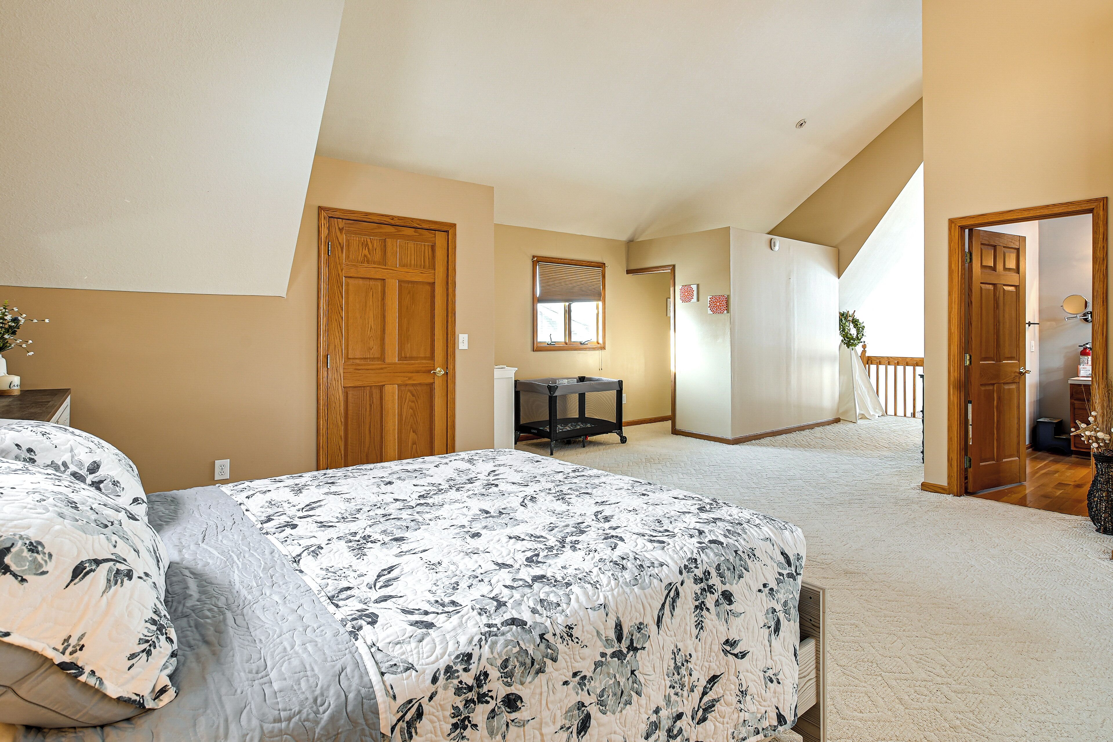 A bedroom with a large bed, a wooden door, a window, and a hallway leading to another room.