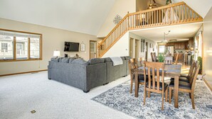 A spacious living room with a grey sectional sofa, wooden dining table with chairs, a staircase, and a kitchen in the background. - Apple Valley Home, Shared Golf Course On-site (Howard)