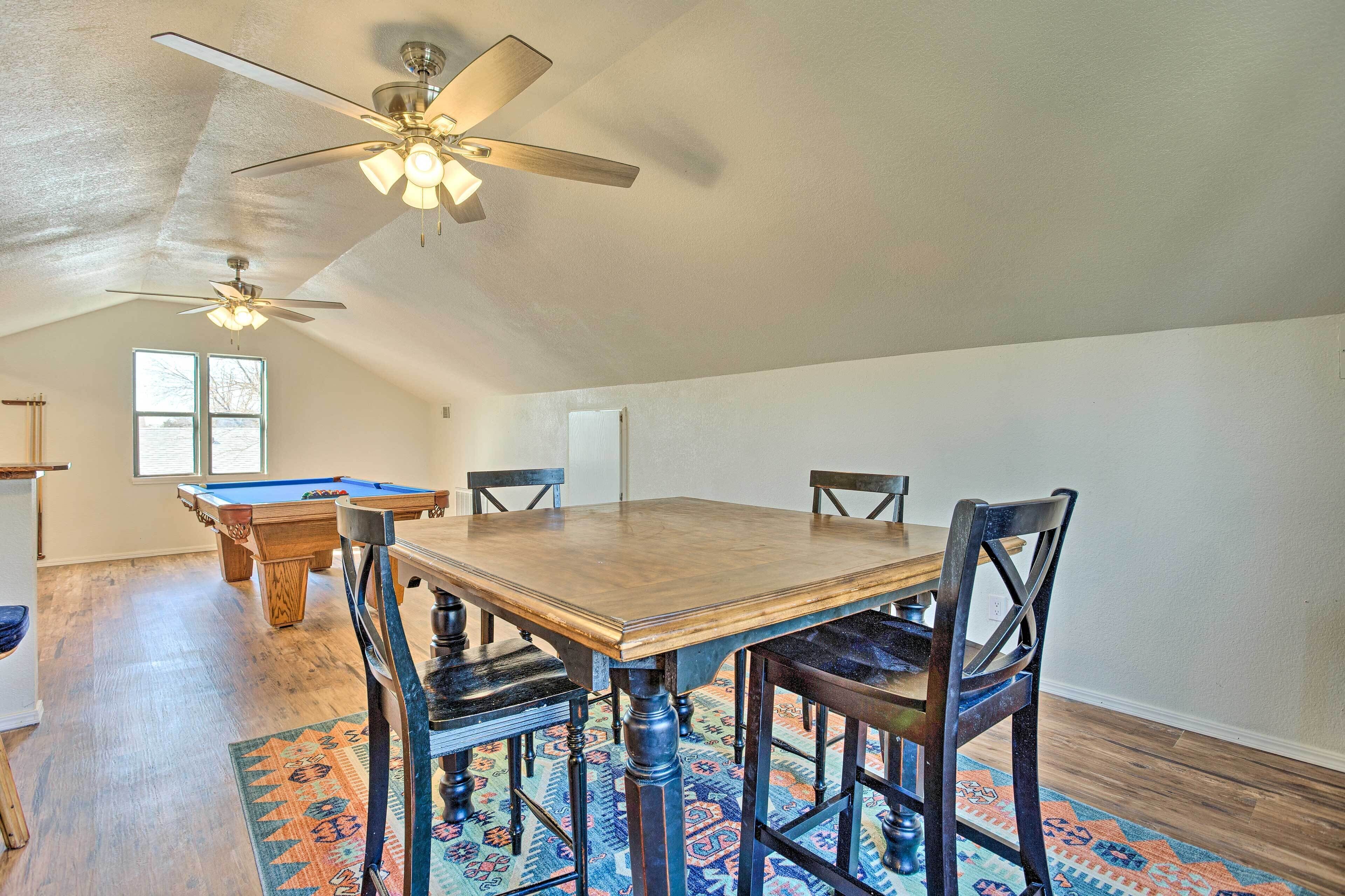 A spacious room with a wooden dining table, four chairs, a pool table, and two ceiling fans.