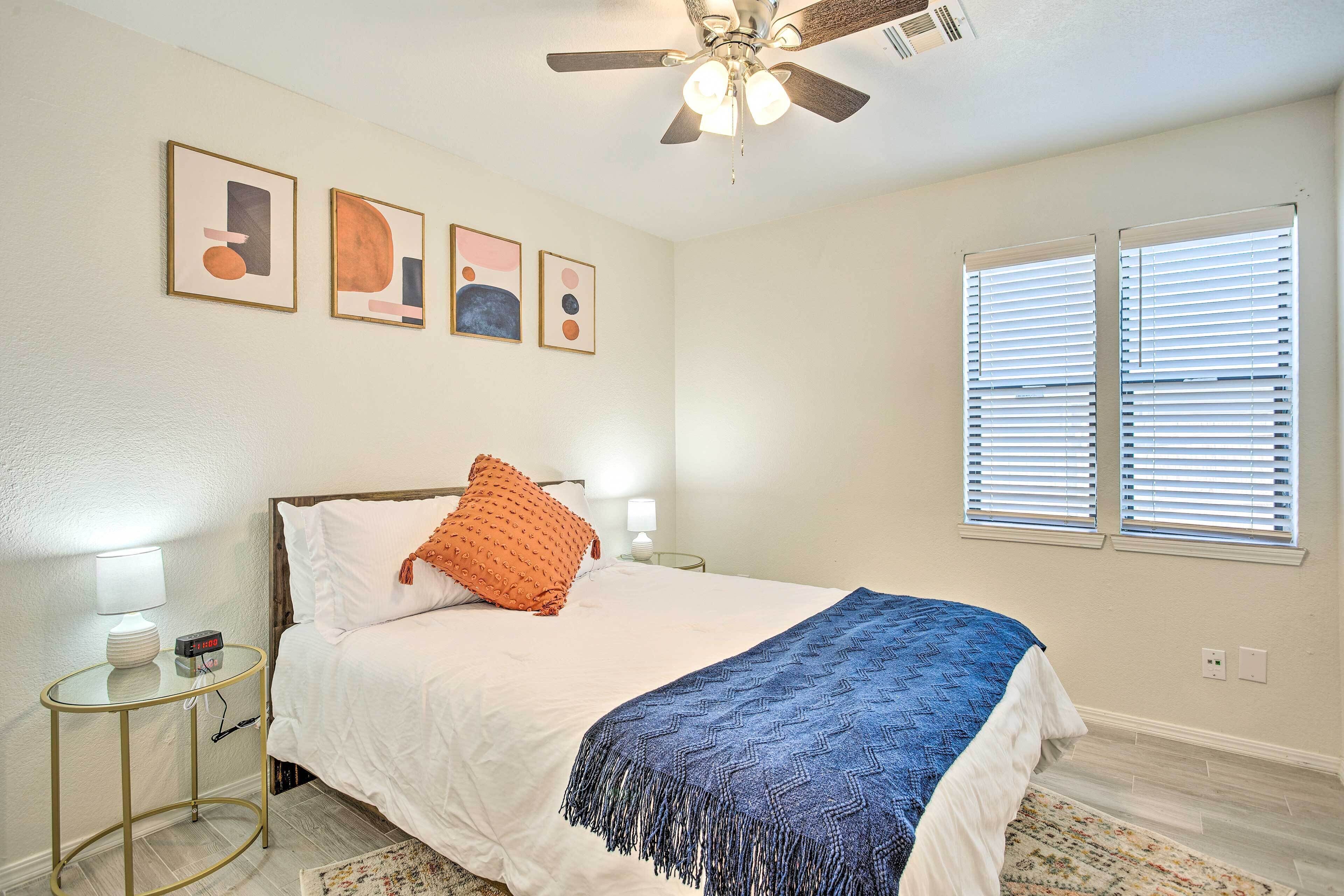 Un dormitorio con cama, ventilador de techo, decoración en la pared y ventana con persianas.