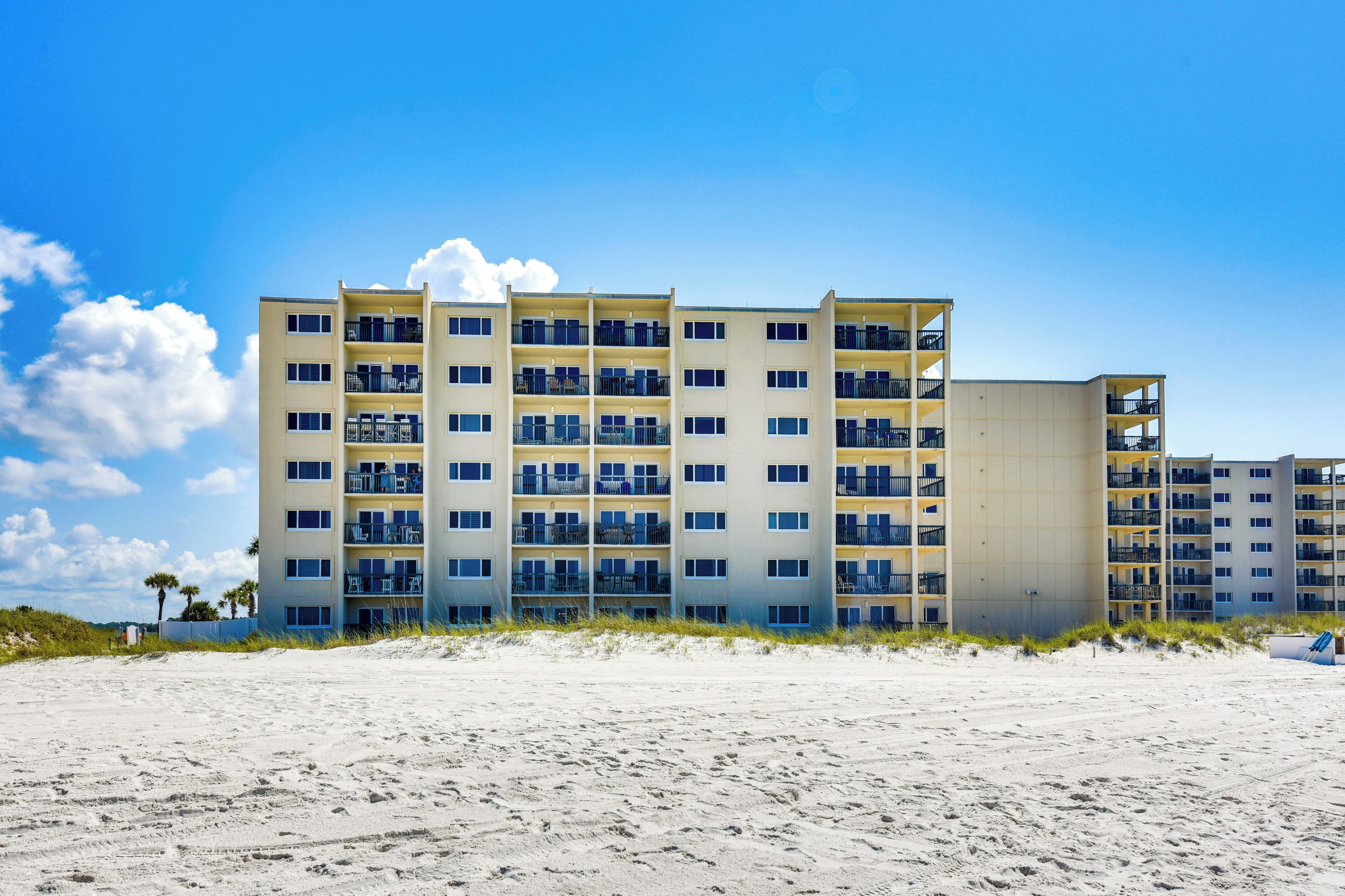 Un hotel de varios pisos con balcones, situado en una playa de arena.