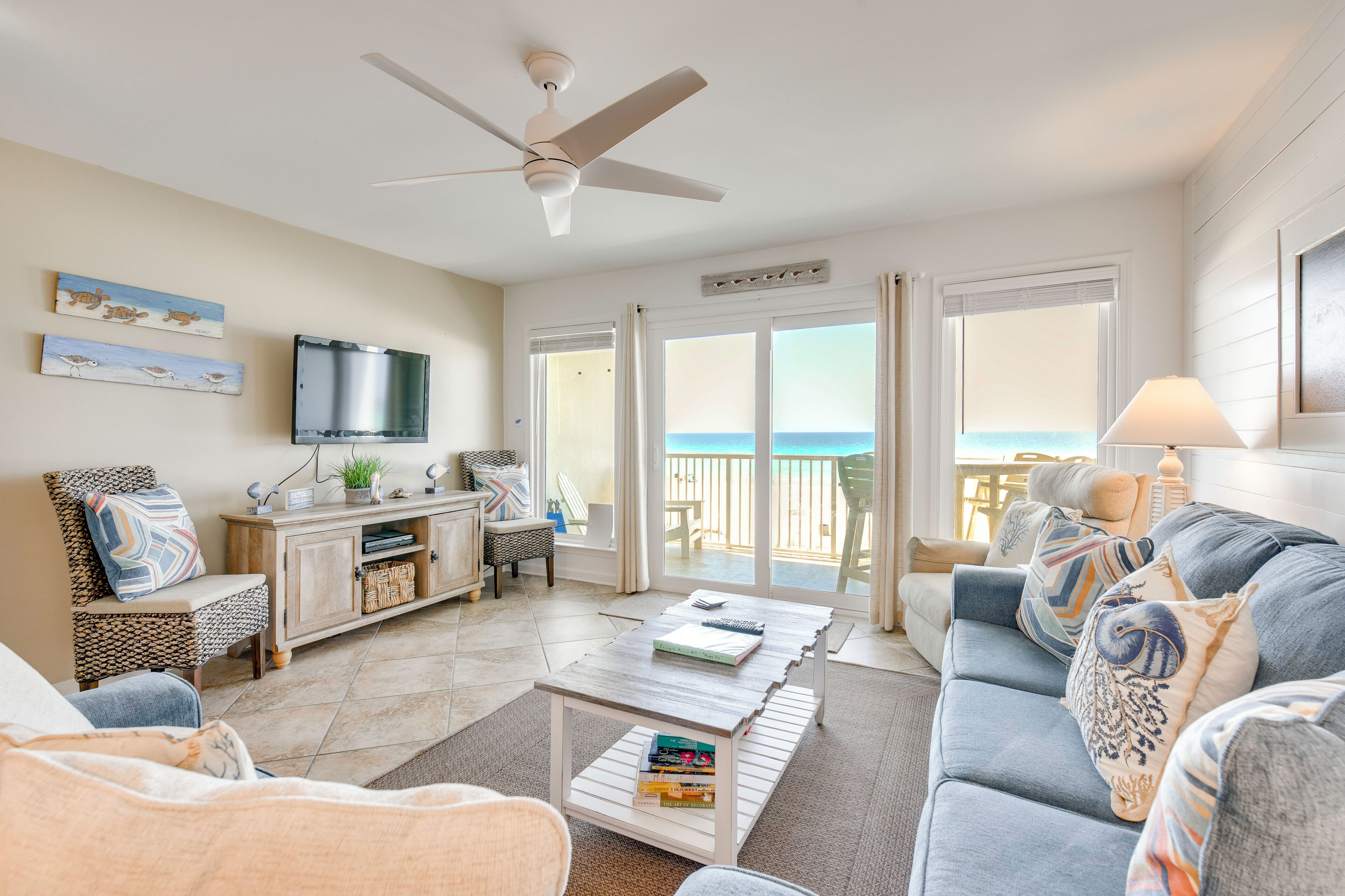 A living room with a sofa, coffee table, TV, and a view of the ocean.