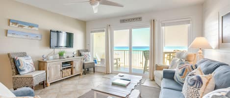 A living room with a sofa, coffee table, TV, and a view of the ocean.