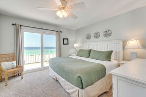 A bedroom with a bed, a chair, a nightstand, a lamp, and a view of the ocean through a sliding door.
