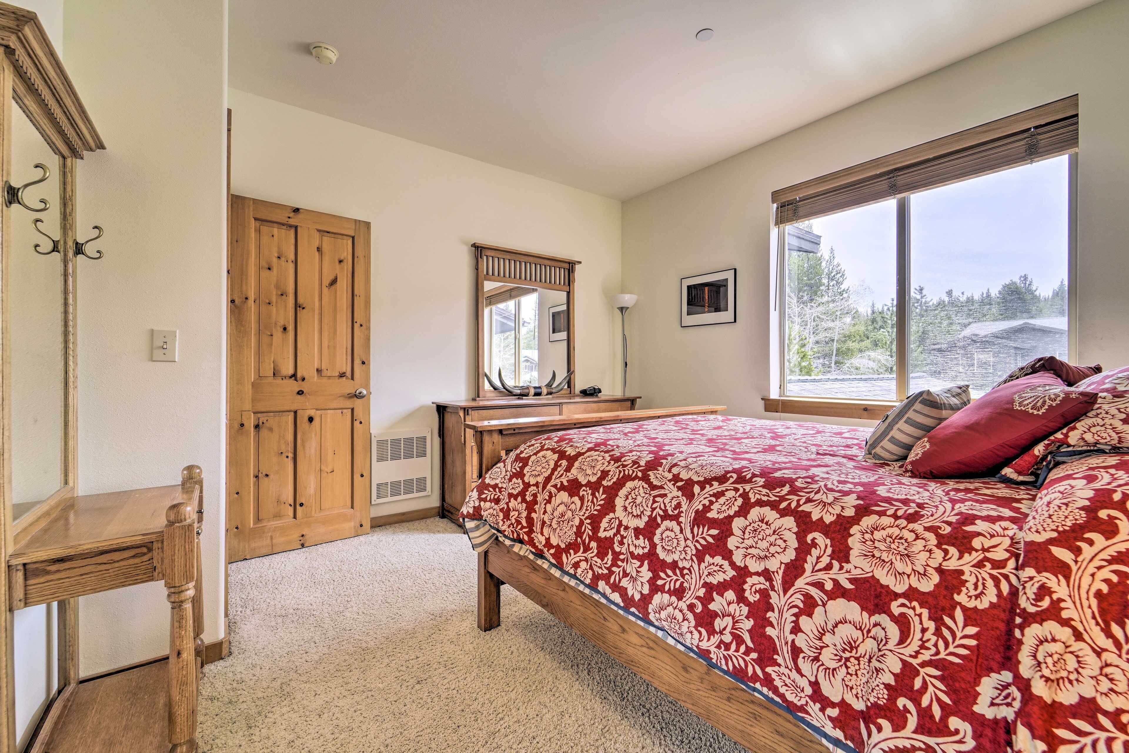 Un dormitorio con una cama de madera, un escritorio, un espejo y una ventana con vista a árboles.
