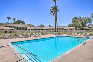 A swimming pool with a clear blue water, surrounded by lounge chairs and a wooden fence. - Patio, Grill + Resort Perks: Palm Desert Home (Palm Desert)