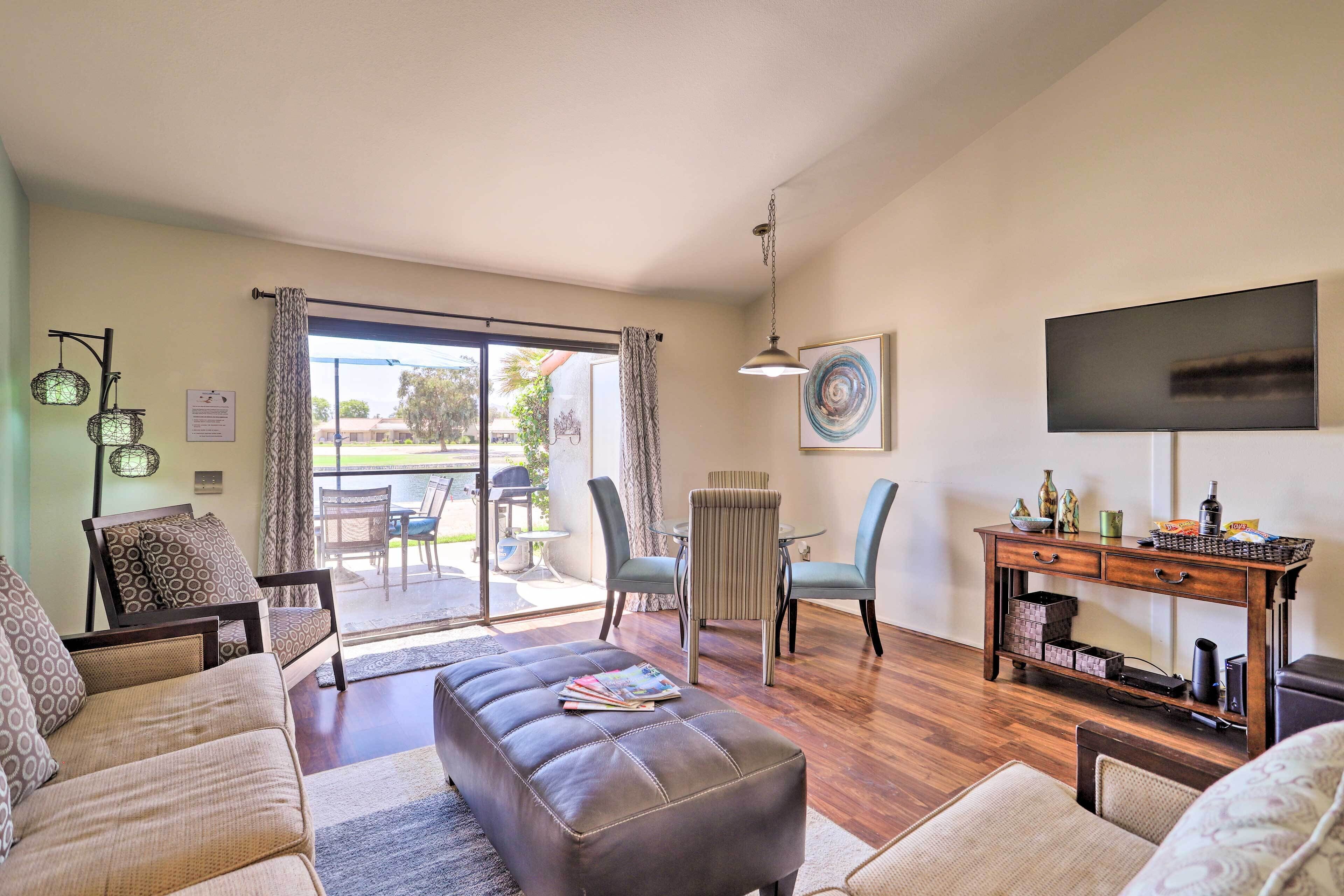 Una sala de estar con sofá, reposapiés y sillas, una mesa de centro de madera, televisor y una zona de comedor con sillas y mesa.