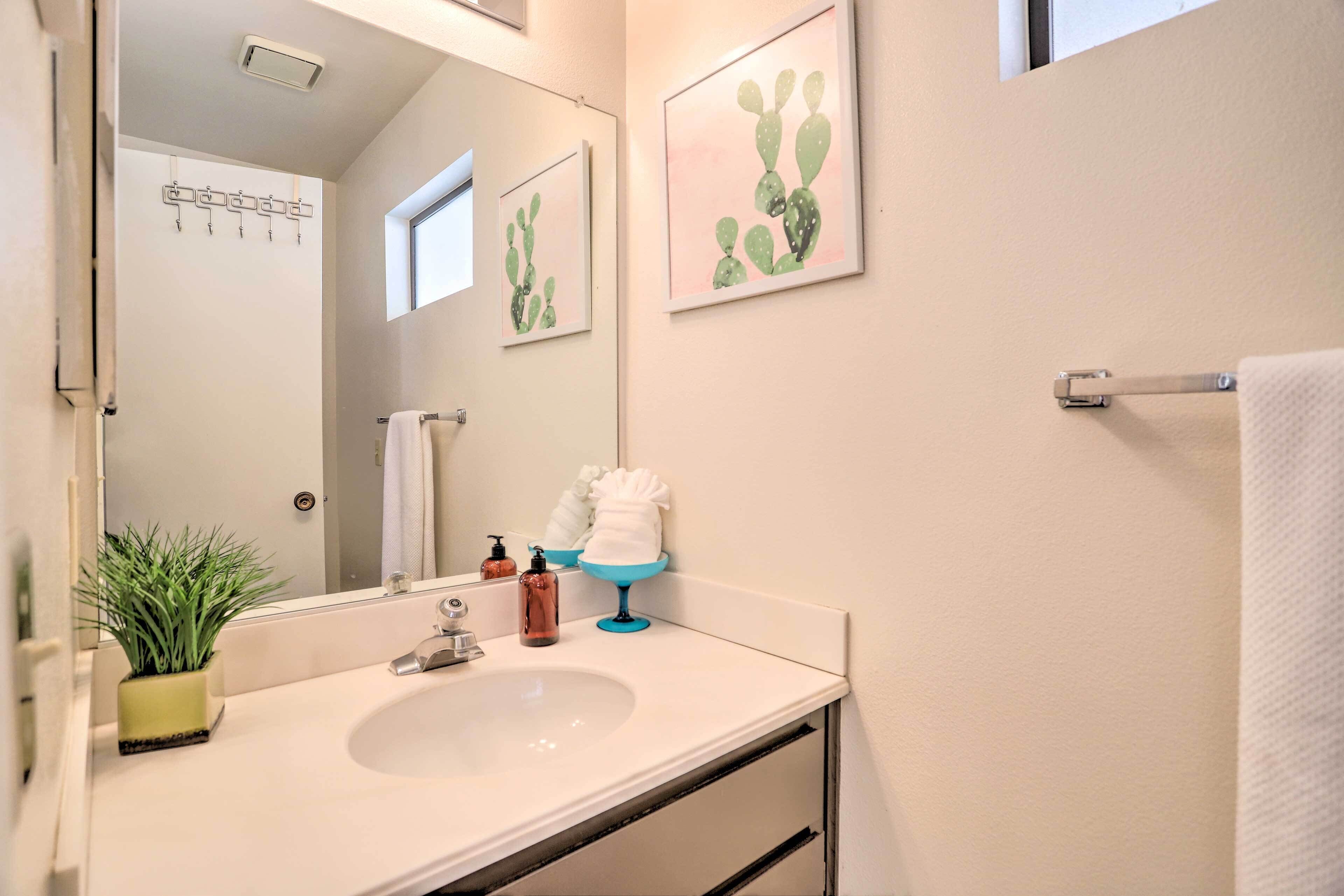 Un baño con lavamanos, espejo, toallero y un cuadro con motivos de cactus.