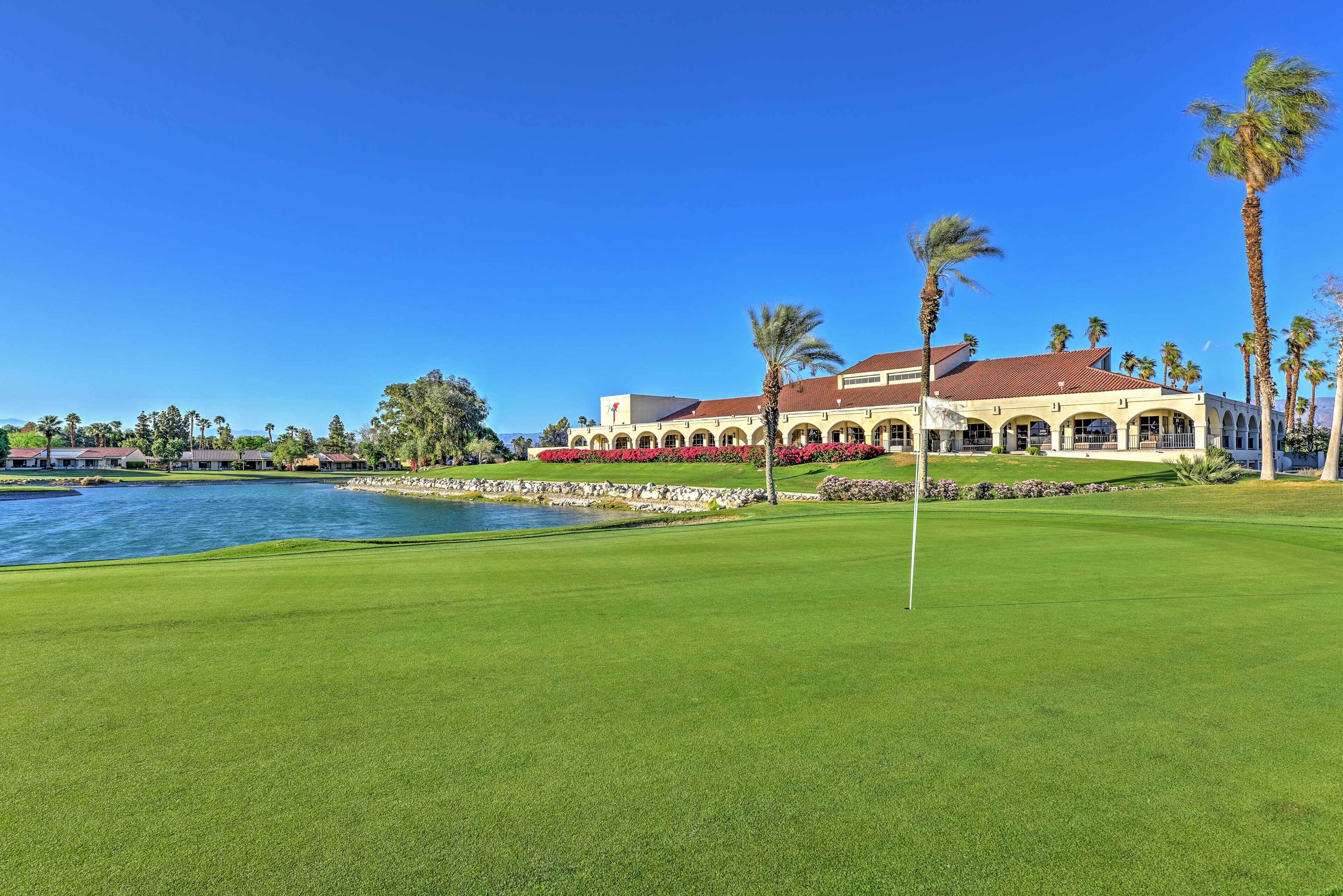 A golf course with a water body, a clubhouse with arches, and palm trees.