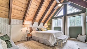 Une chambre à coucher avec un grand lit, une table de chevet, une lampe et une vue sur l’extérieur par les fenêtres.