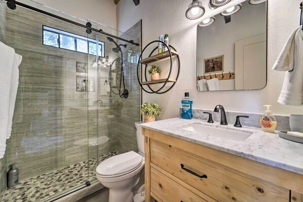 A modern bathroom with a glass shower enclosure, a white toilet, a marble sink, and wooden cabinets.