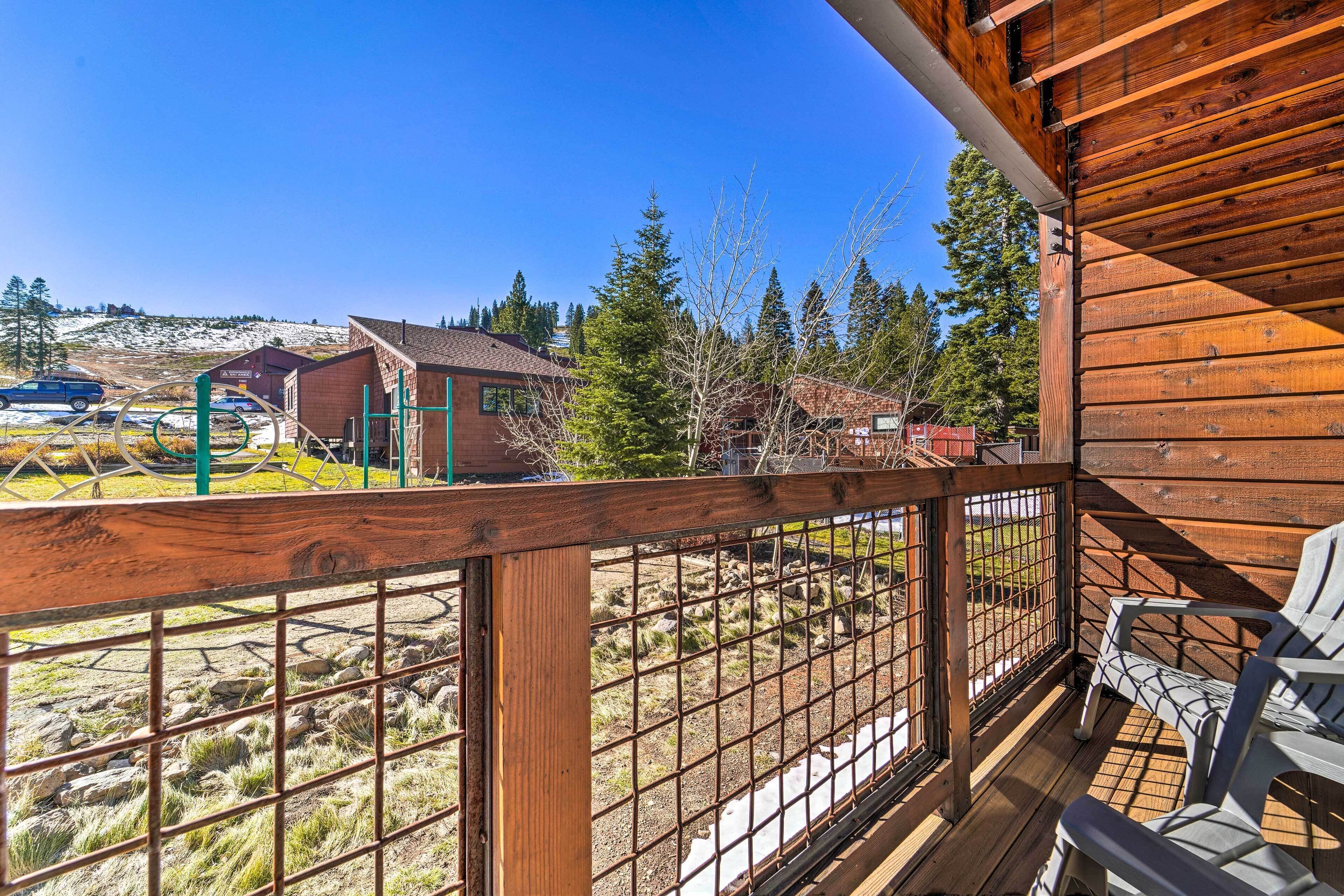 A wooden deck with a metal railing, a view of a rural landscape with houses and trees, and two white chairs.