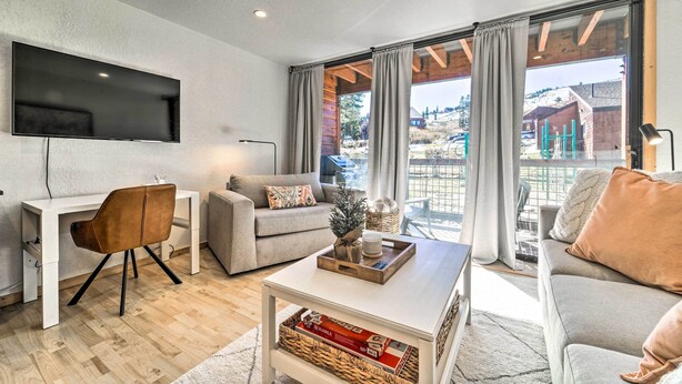A modern living room with a flat-screen TV, a white desk, a grey sofa, and a coffee table with a tray. - Walk to Ski Resort: Tahoe Donner Studio w/ Balcony (Truckee)