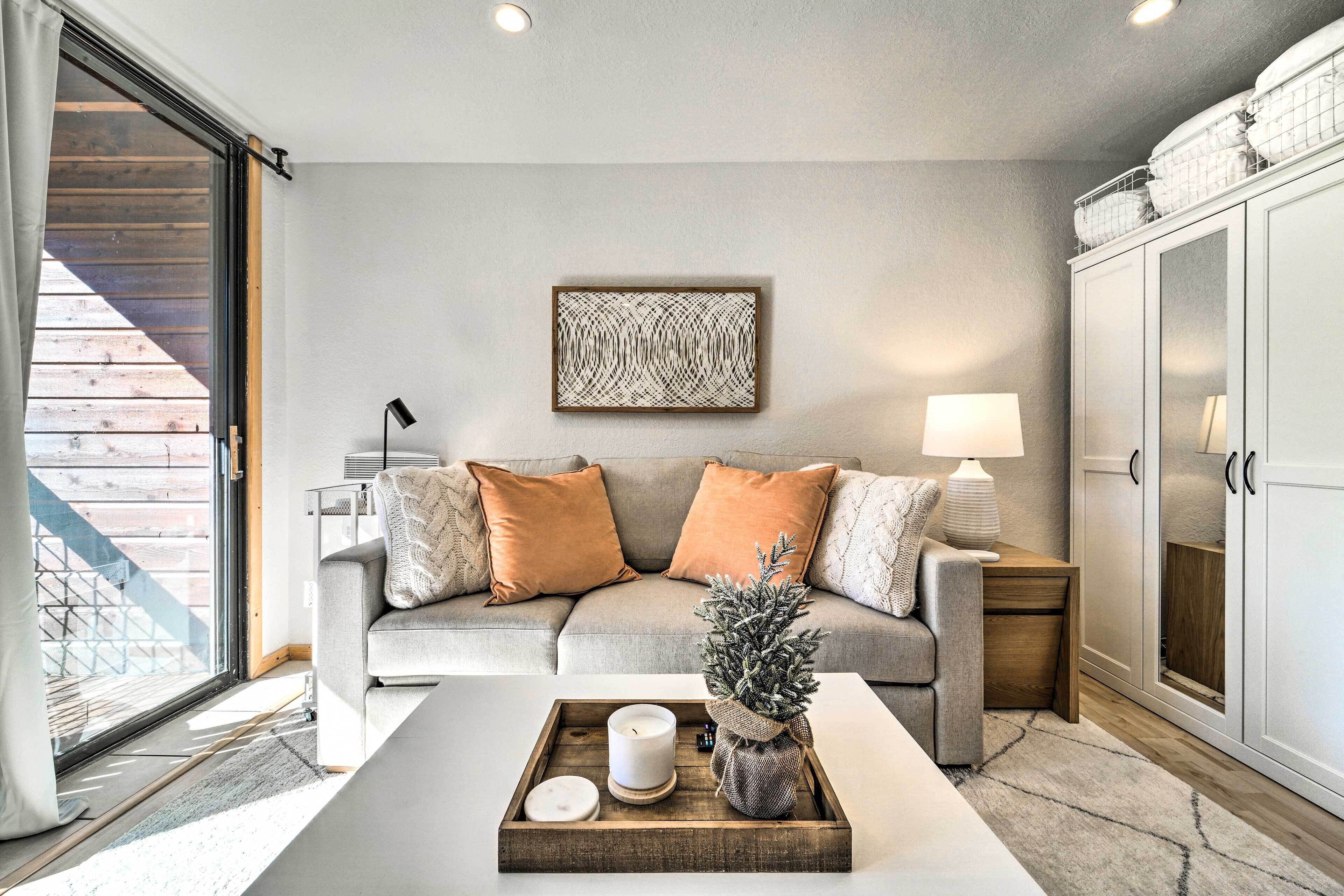 A modern living room with a grey sofa, orange cushions, a coffee table with candles, and a decorative tree.
